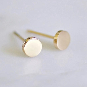 Minimalist round polished gold stainless steel stud earrings on a grey stone surface