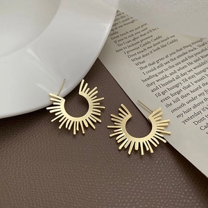 Minimalist gold sunburst stud earrings displayed on a textured leather and ceramic background