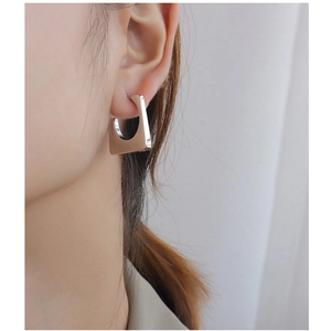 Macro detail of polished silver trapezoid earrings worn on ear showing glossy metal finish