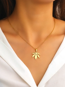 Close-up of a delicate gold maple leaf pendant necklace worn on a white V-neck top