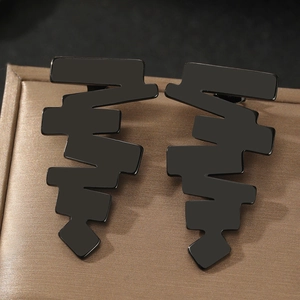 Detail of matte black geometric earrings with jagged wave design on brown satin padding