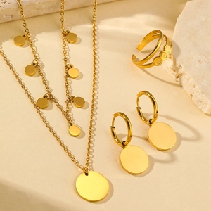 Minimalist multilayer gold necklace and earring set on a beige stone background