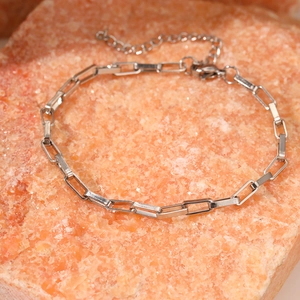 Détail du bracelet à maillons trombone argentés avec fermoir sur fond de pierre orange