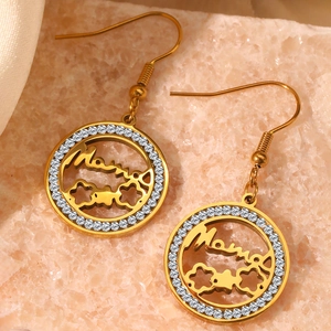 Detail of golden Mama earrings with white rhinestones on soft satin background