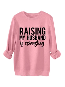 Close-up of pink crewneck sweatshirt featuring black 'RAISING MY HUSBAND' slogan print