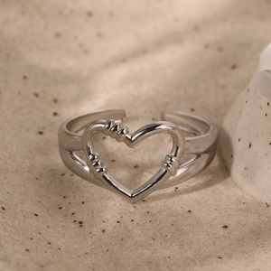 Minimalist silver open ring with hollow heart design and rope texture on sand background