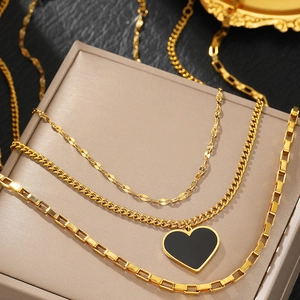 Collier doré à trois rangs avec pendentif cœur noir sur un coffret à bijoux