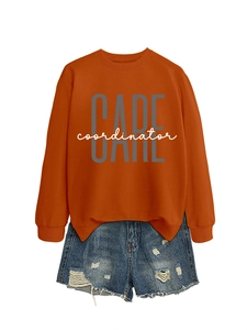 Detail of rust red sweatshirt with CARE coordinator print and distressed denim shorts
