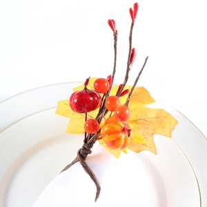 Detail of autumn napkin ring featuring artificial maple leaf, pumpkin, and berries on a plate