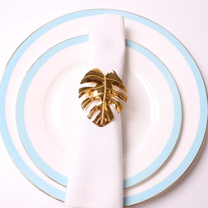 Detail of golden monstera leaf napkin ring on a white napkin over ceramic plates