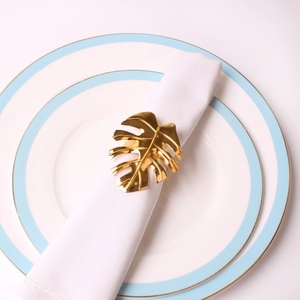 Golden Monstera leaf napkin ring on white fabric napkin and elegant ceramic plate