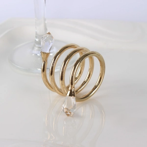 Spiral gold metal napkin ring with crystal beads on a white ceramic plate background