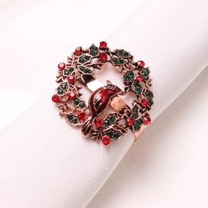 Close-up of a metal Christmas napkin ring featuring a red bird and holly leaves wreath
