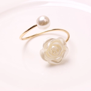 Elegant gold napkin ring with white rose and pearl accents on a minimalist plate
