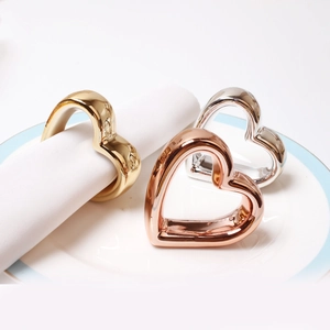 Elegant heart-shaped napkin rings in gold, silver, and rose gold on a white ceramic plate