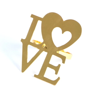 Detailed close-up of golden metal LOVE napkin ring with polished hollow heart design