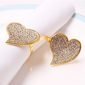 Close-up of golden heart-shaped napkin rings with white rhinestones on white cotton napkins