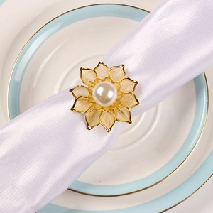 Detail of a golden lotus napkin ring with a white pearl on a white satin napkin