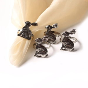 Detailed view of four vintage silver rabbit napkin rings on a smooth yellow fabric cloth