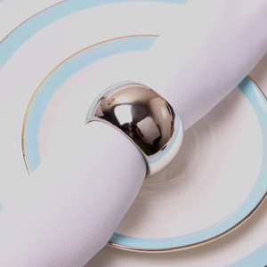 Dettaglio di un portatovagliolo in argento lucido su un tovagliolo e piatto in ceramica