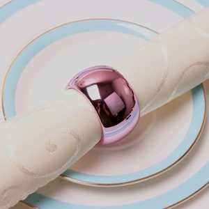 Dettaglio di un portatovagliolo in metallo rosa lucido su tovagliolo e piatto bianco