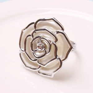 Silver rose flower napkin ring with white enamel petals on a ceramic surface
