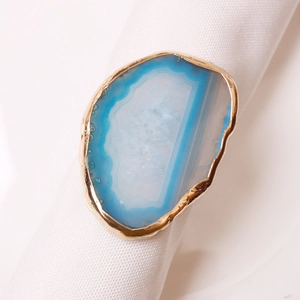 Blue natural agate slice napkin ring with gold plated edges on white fabric