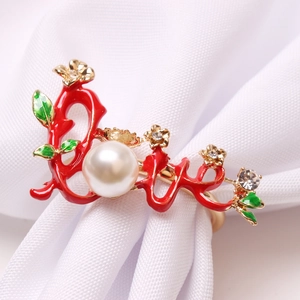 Close-up of golden Love napkin ring with red enamel, pearl and sparkling crystals