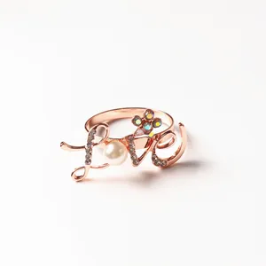 Macro detail of rose gold LOVE napkin ring with white pearl and rhinestone flower