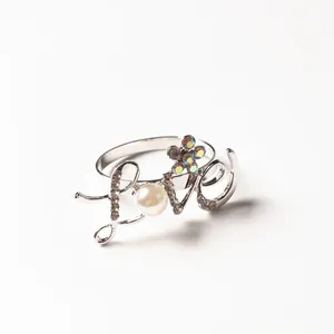 Macro detail of silver 'Love' napkin ring with iridescent flower and pearl accent
