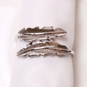 Polished silver double feather napkin ring with intricate texture on a white cloth napkin