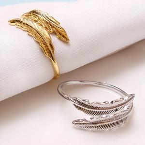 Detail of elegant gold and silver metal feather napkin rings on white linens