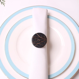 Detail of copper wire wrapped black marble napkin ring on white fabric and porcelain plate