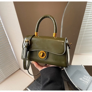 Close-up of dark green glossy leather handbag with elegant gold ring lock and top handle