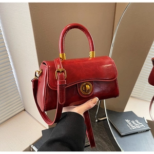 Detailed view of dark red glossy leather handbag with gold twist lock and handle