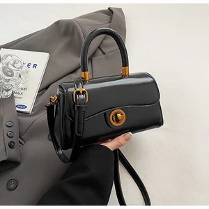 Detail of a black leather crossbody bag featuring a vintage round gold twist lock closure