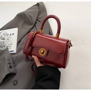 Detail of burgundy leather handbag with golden twist lock on grey suit background