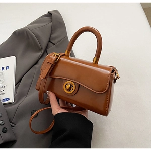 Detail of vintage brown leather handbag featuring a golden circular twist lock and handle