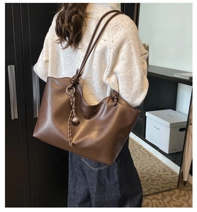 Detail of dark brown tote bag featuring knotted straps and a metallic ball pendant charm