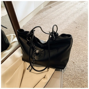 Detail of black leather tote bag featuring elegant shoulder strap knots and metal bead accents