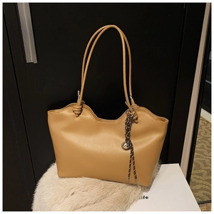 Detail of camel tote bag with wave-cut edges and decorative bell charm on plush surface