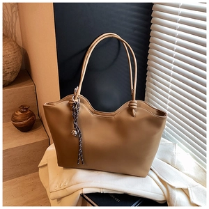 Detailed view of camel tote bag with knot straps and bell charm on stone steps