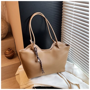 Detailed view of khaki tote bag with bell pendant and scalloped edge on white suit jacket