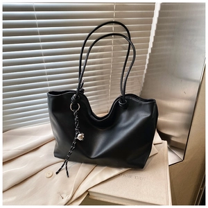 Detail of black faux leather tote bag with unique V-shaped rim and woven tassel charm