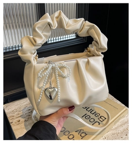 Detail of creamy white pleated handbag with faux pearl bow and silver heart charm decoration