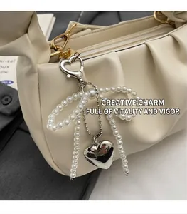 Close-up of decorative pearl bow and metal heart pendant on beige ruched shoulder bag