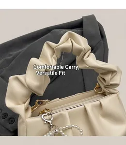 Detail of cream pleated handbag with golden zipper and heart pearl charm accessory