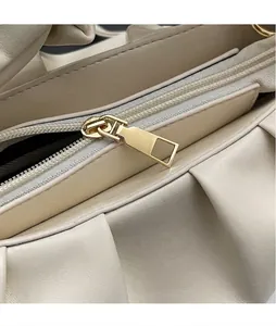 Detailed close-up of beige pleated leather handbag with polished gold-tone hardware zipper