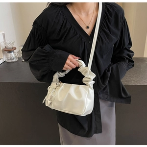 Detail of white pleated cloud bag with pearl butterfly and silver heart charms on shoulder strap