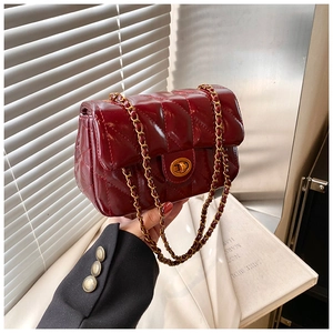 Gros plan du sac en cuir verni matelassé bordeaux avec chaîne dorée et fermoir rotatif